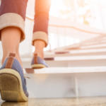 Young adult woman walking up the stairs with sun sport background.