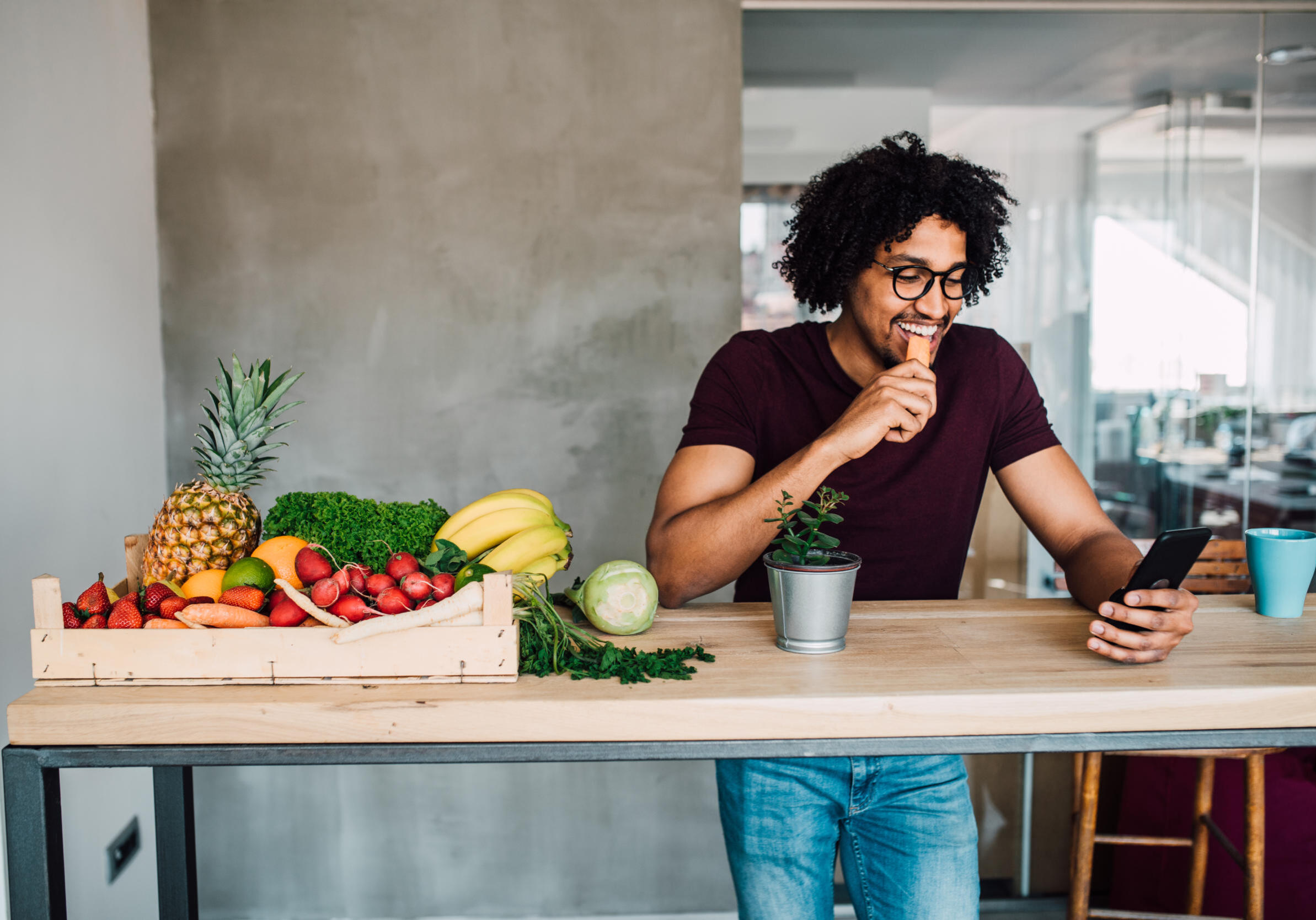 Young man having a healthy snack at home when using phone