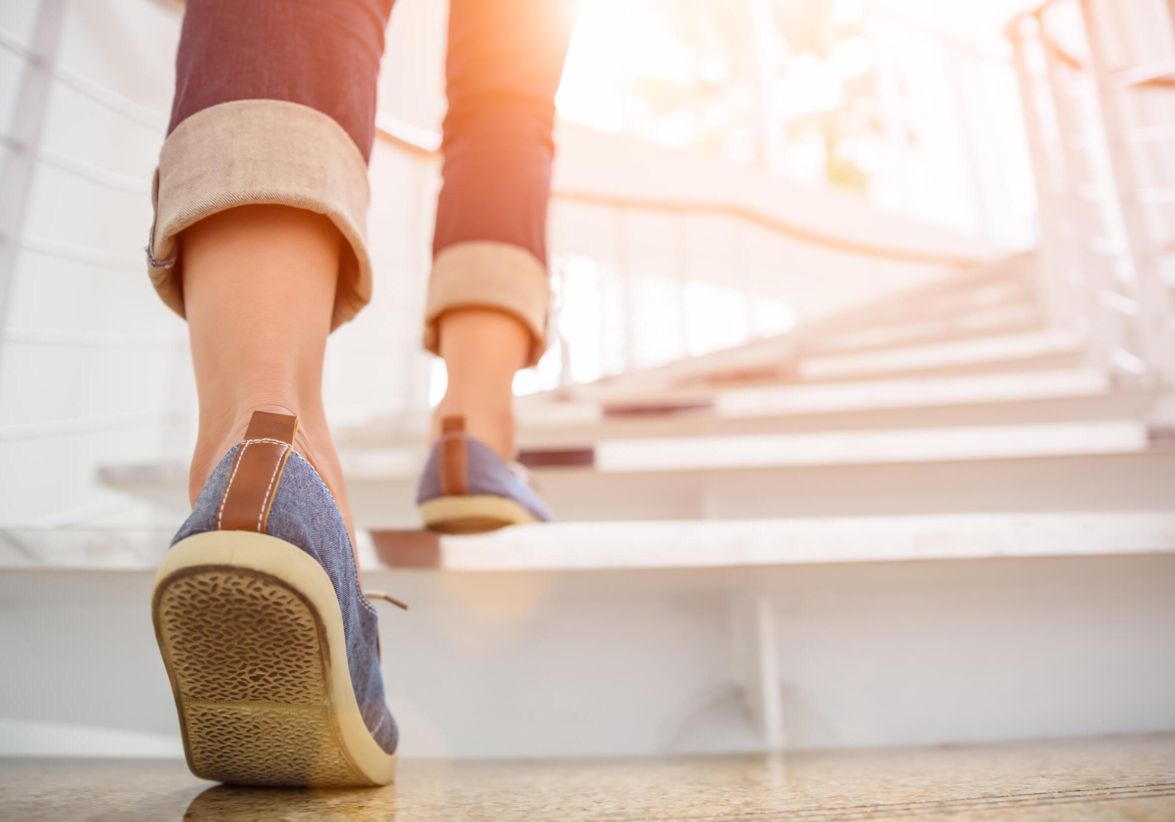 Young adult woman walking up the stairs with sun sport background.